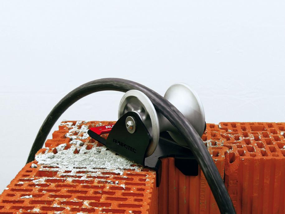 The cable guide roller - shaft inside edge is ideally suited for mounting on the edge of a shaft or on steps to pull cables gently around corners with the least possible resistance. Example photo showing roller mounted to the corner of a brick wall.